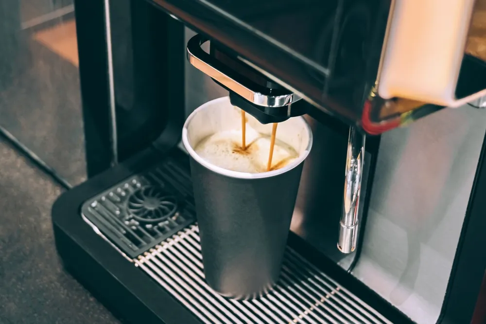 Espresso machine pouring hot coffee into a paper cup